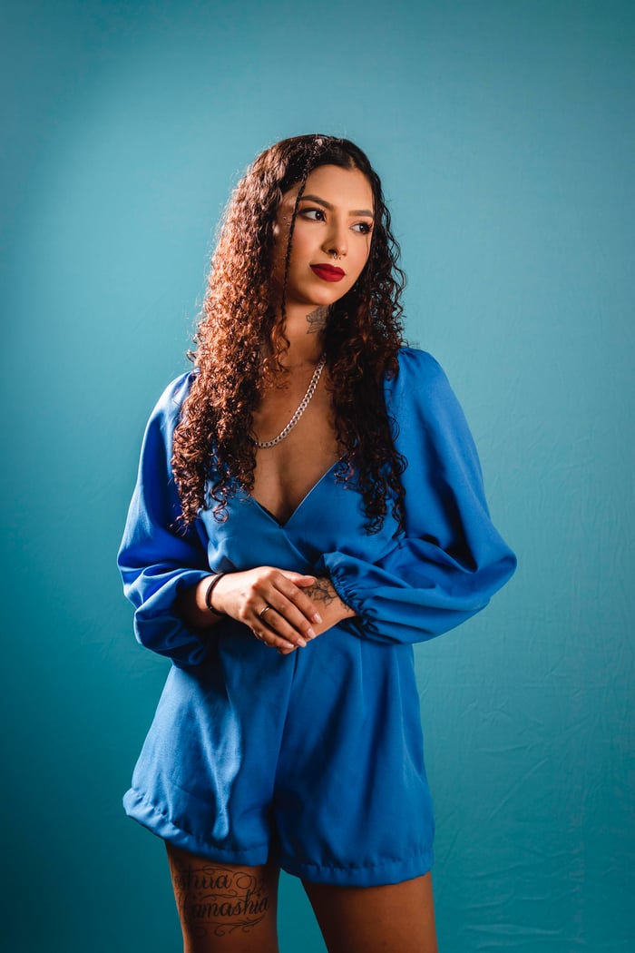 About Stylish portrait of a young woman posing confidently in a blue romper with a blue background.